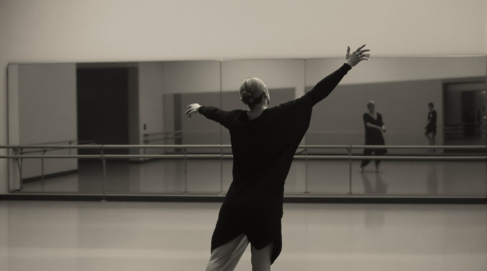 A choreographer marking a movement phrase alone in a mirrored studio