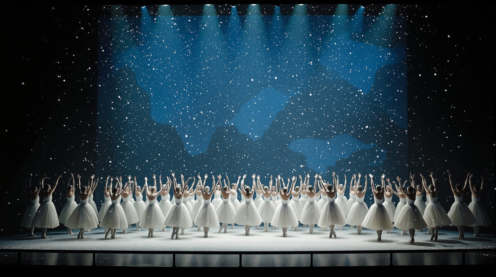 The snow scene of a Nutcracker production, dancers in white tutus silhouetted against a blue winter backdrop with falling stage snow