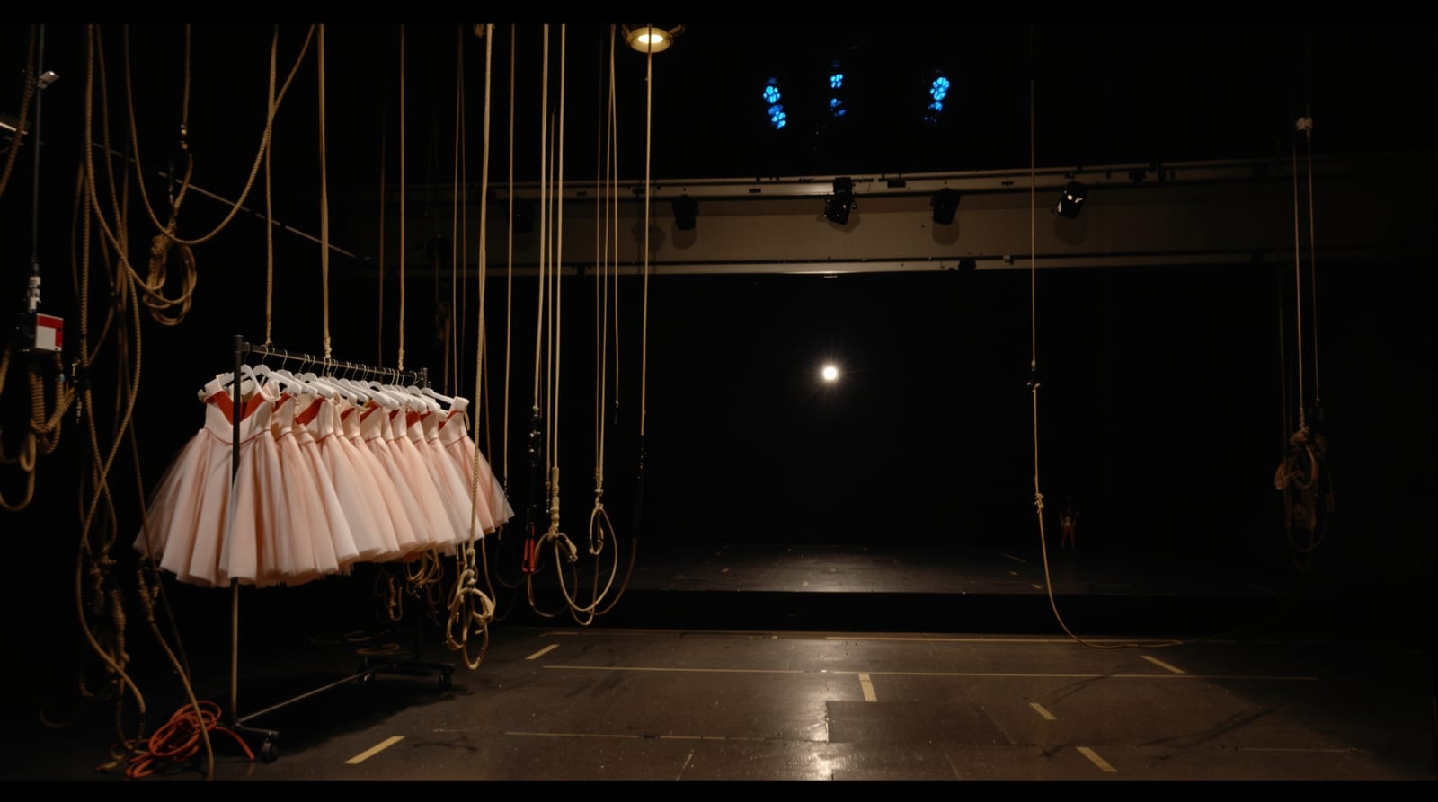 The wings of a theatre during technical rehearsal, with a counterweight rail, a costume rack and taped stage floor beyond